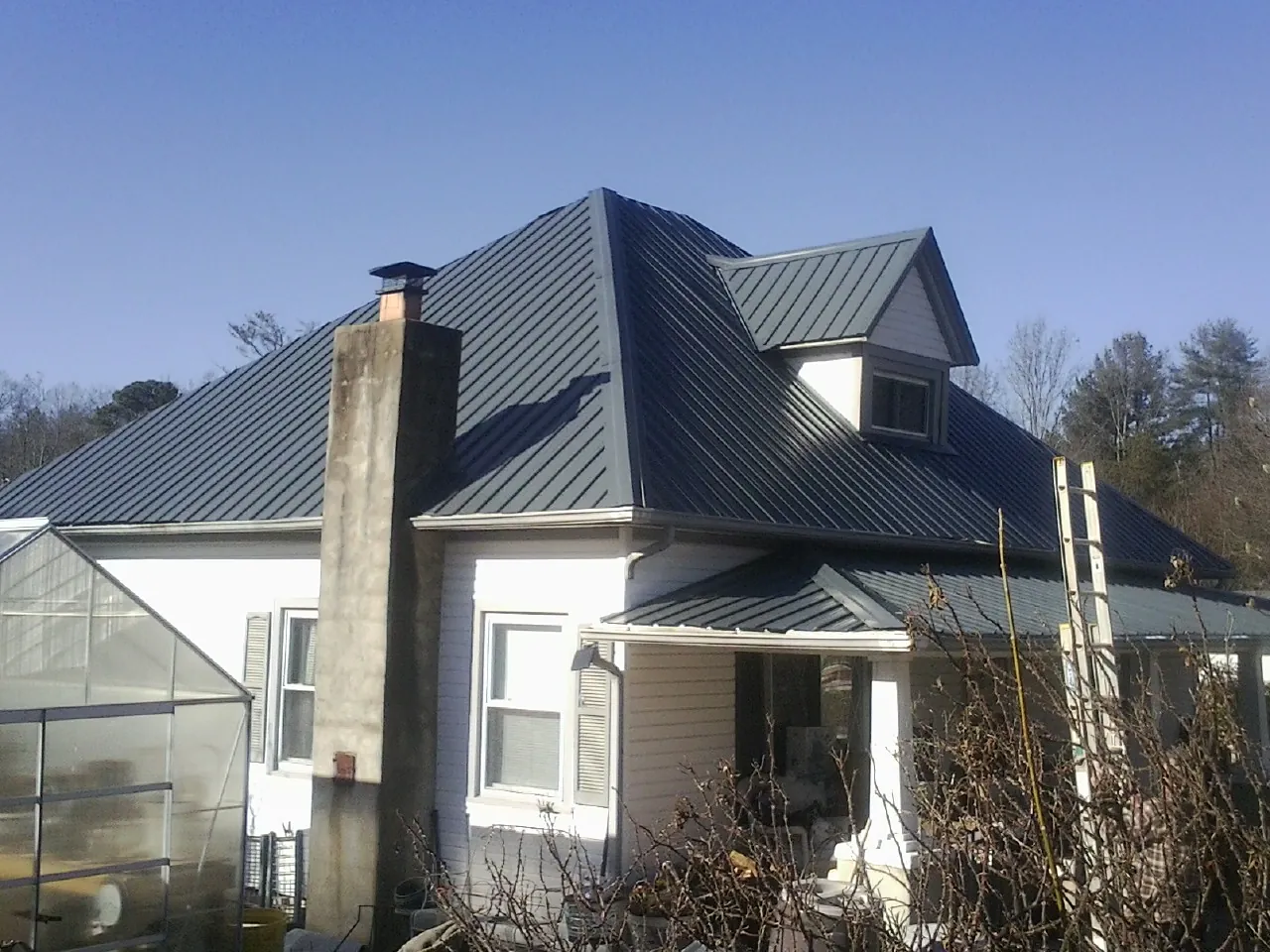 Dark blue standing seam metal roof on a white farmhouse with dormer — Slate & Tile Roof Repair by Roofing Brothers in Bastrop