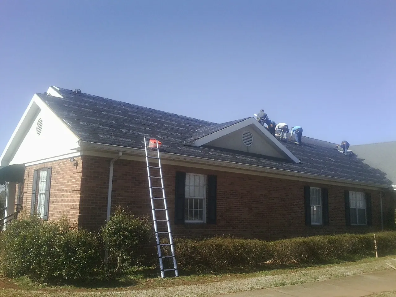Crew tearing shingles off a brick ranch roof with a ladder set — Emergency Roof Repair work by our crew in Bastrop