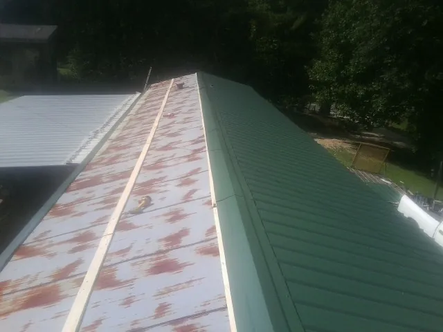 Old rusted panels beside newly installed green metal roofing — Wind Damage Roof Repair by Roofing Brothers in Bastrop