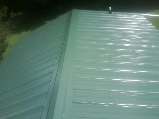 New green metal panels meeting at the ridge of a roof — Flat Roof Repair work by our crew in Bastrop