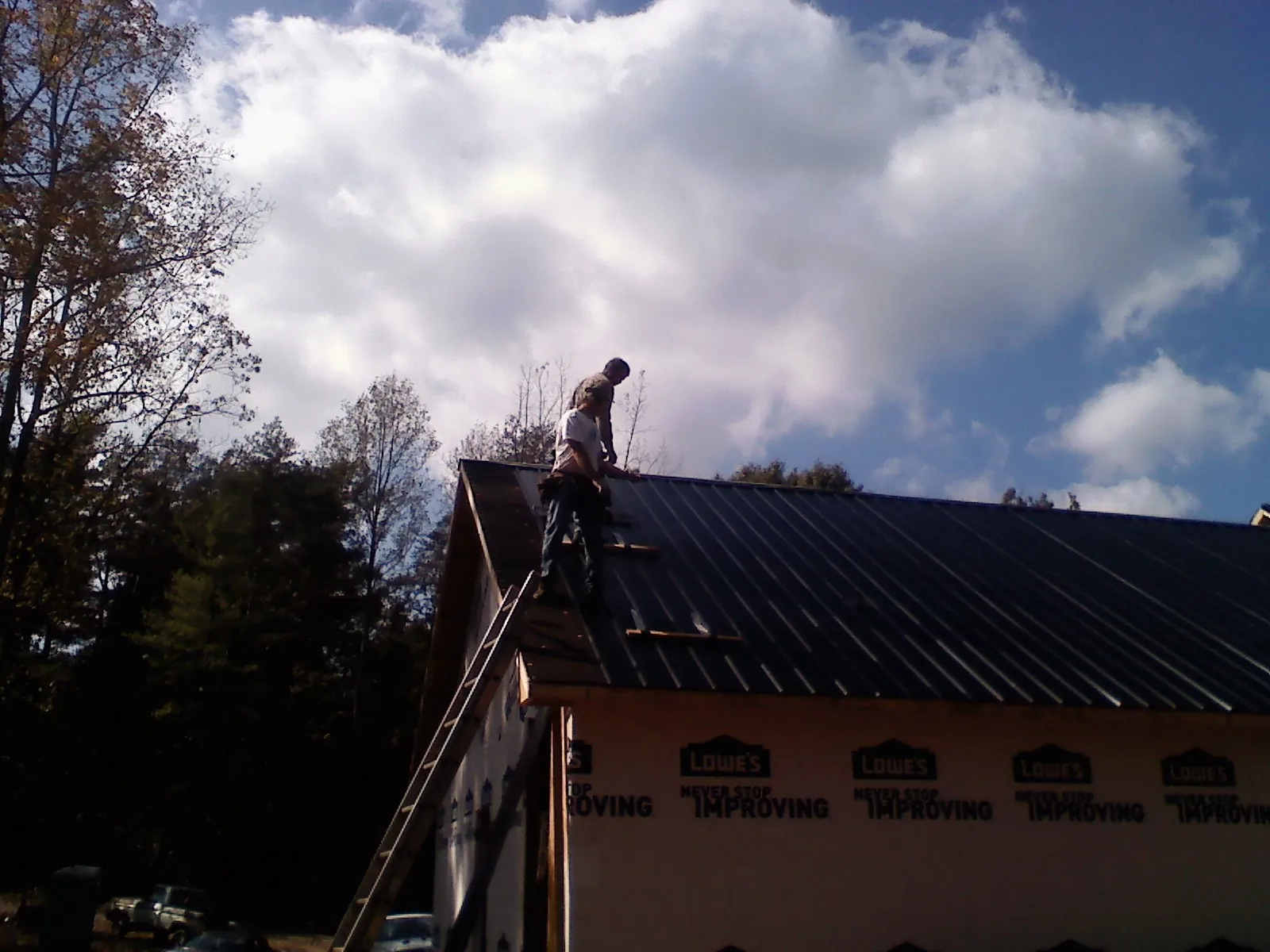Roofer fastening dark metal panels high against a cloudy sky, from a Roof Inspection job in Bastrop