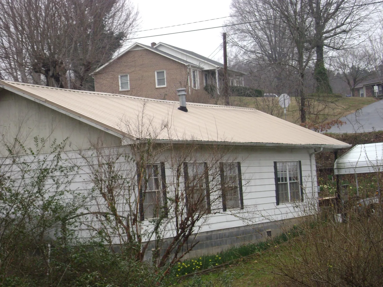 Tan metal roof on a white sided house set into a hillside — Commercial Roofing by Roofing Brothers in Bastrop