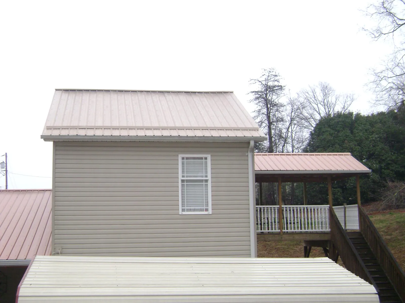 Tan metal roofs on a two story addition and attached porch, from a Roof Replacement job in Bastrop