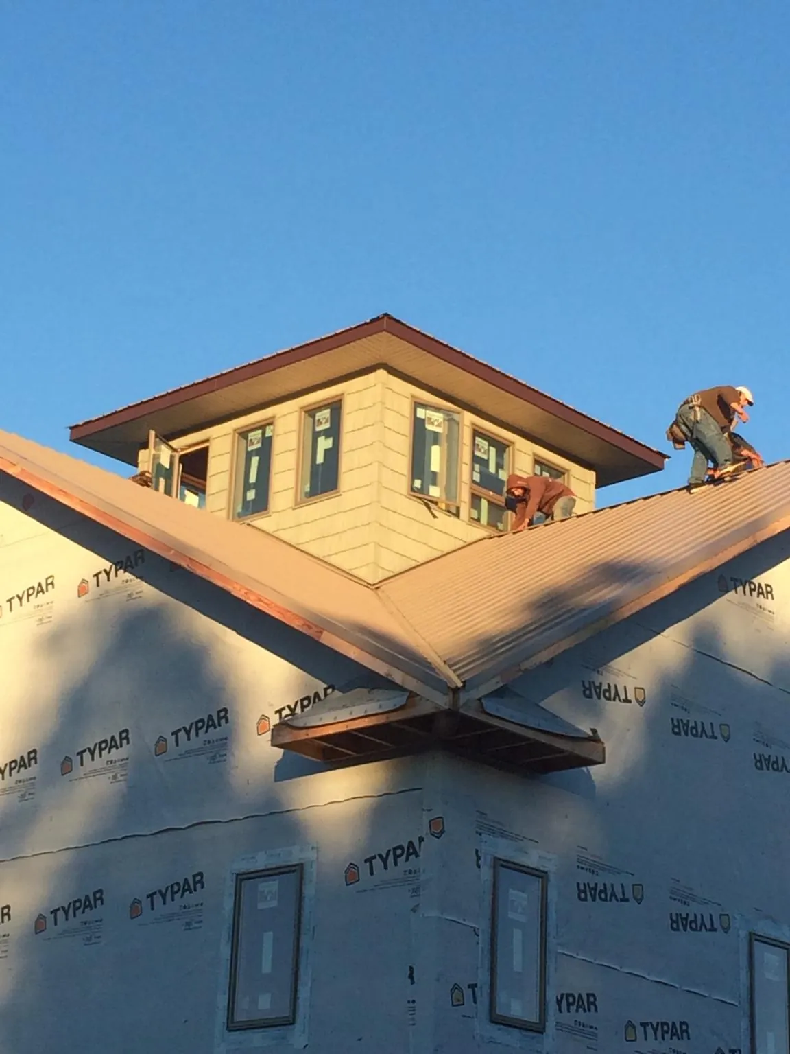 Roofers working around a rooftop cupola on a new metal roof at sunset — Roof Waterproofing in Bastrop by Roofing Brothers